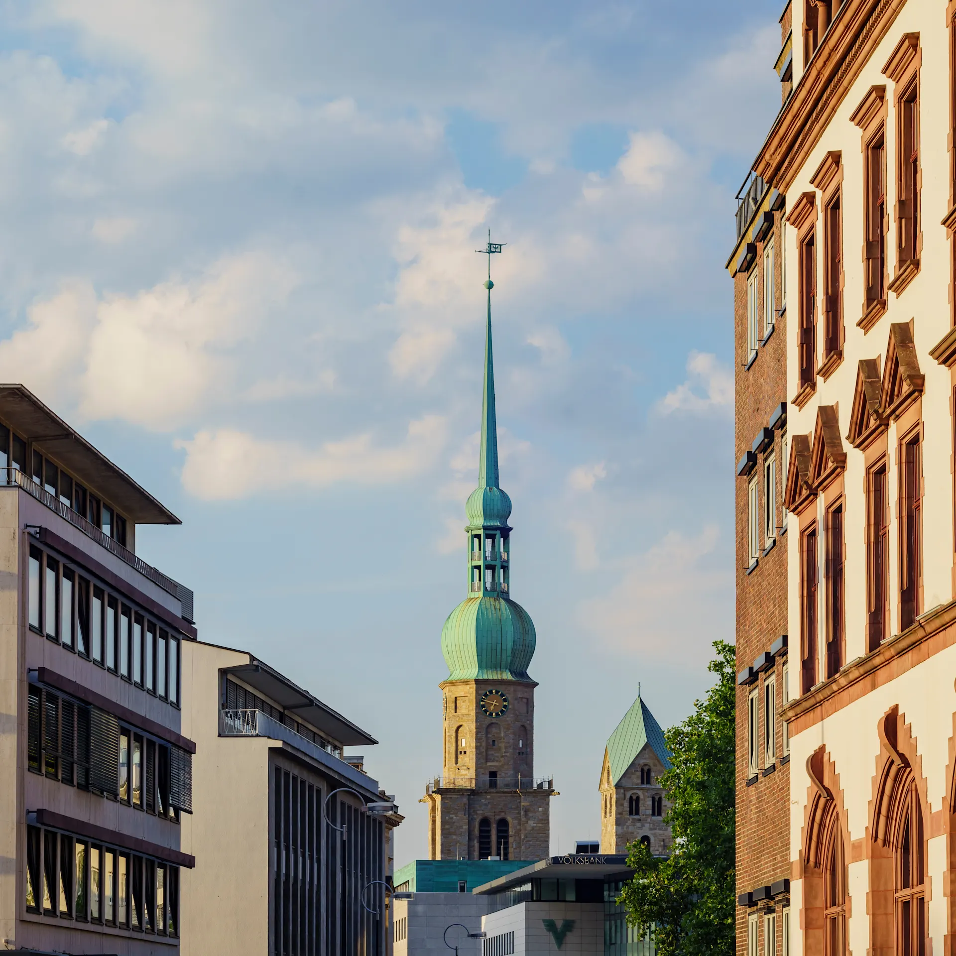 Blick auf eine Straße mit modernen und historischen Gebäuden, Kirchturm im Hintergrund.