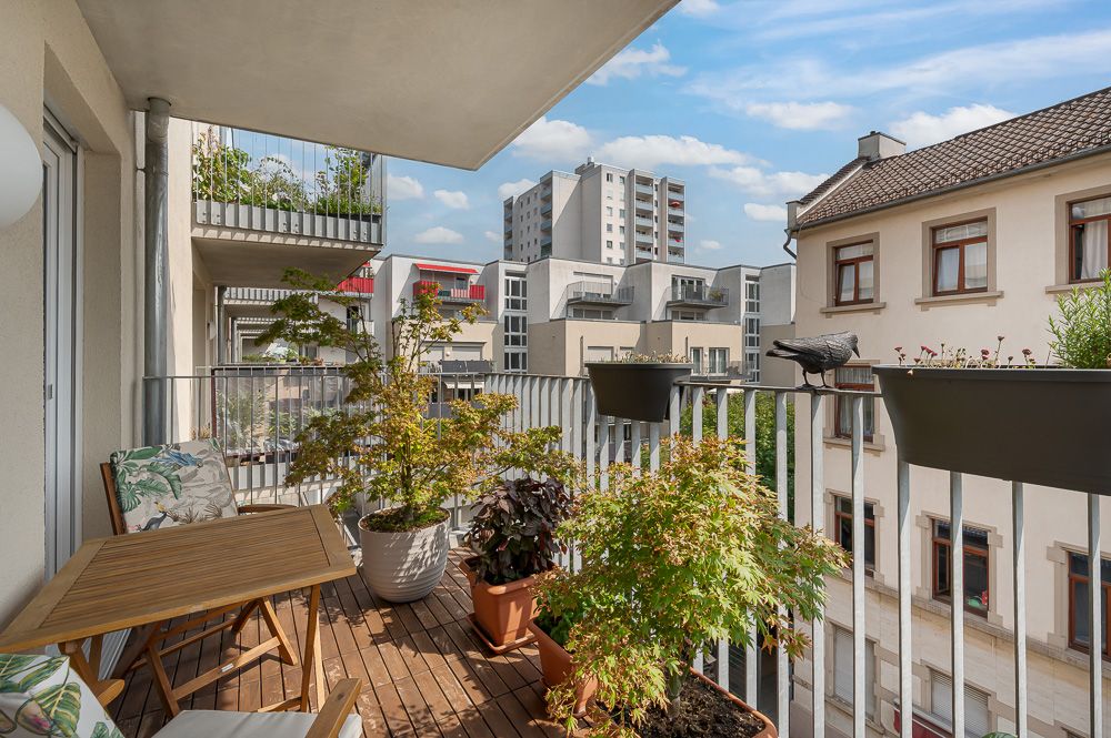 Balkon mit Holzboden, Pflanzen, Tisch, Stühlen und Blick auf Nachbargebäude.