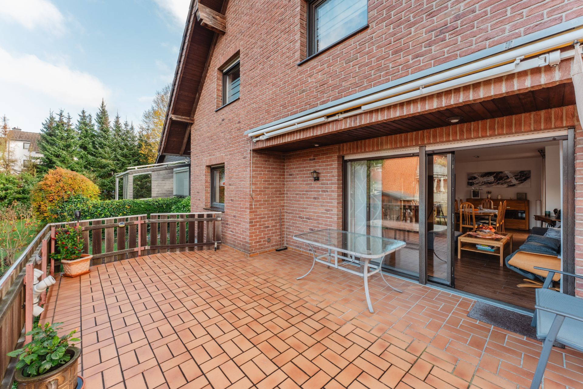 Große Terrasse mit Glastisch an einem Backsteinhaus, Zugang zum Wohnzimmer durch Schiebetüren.