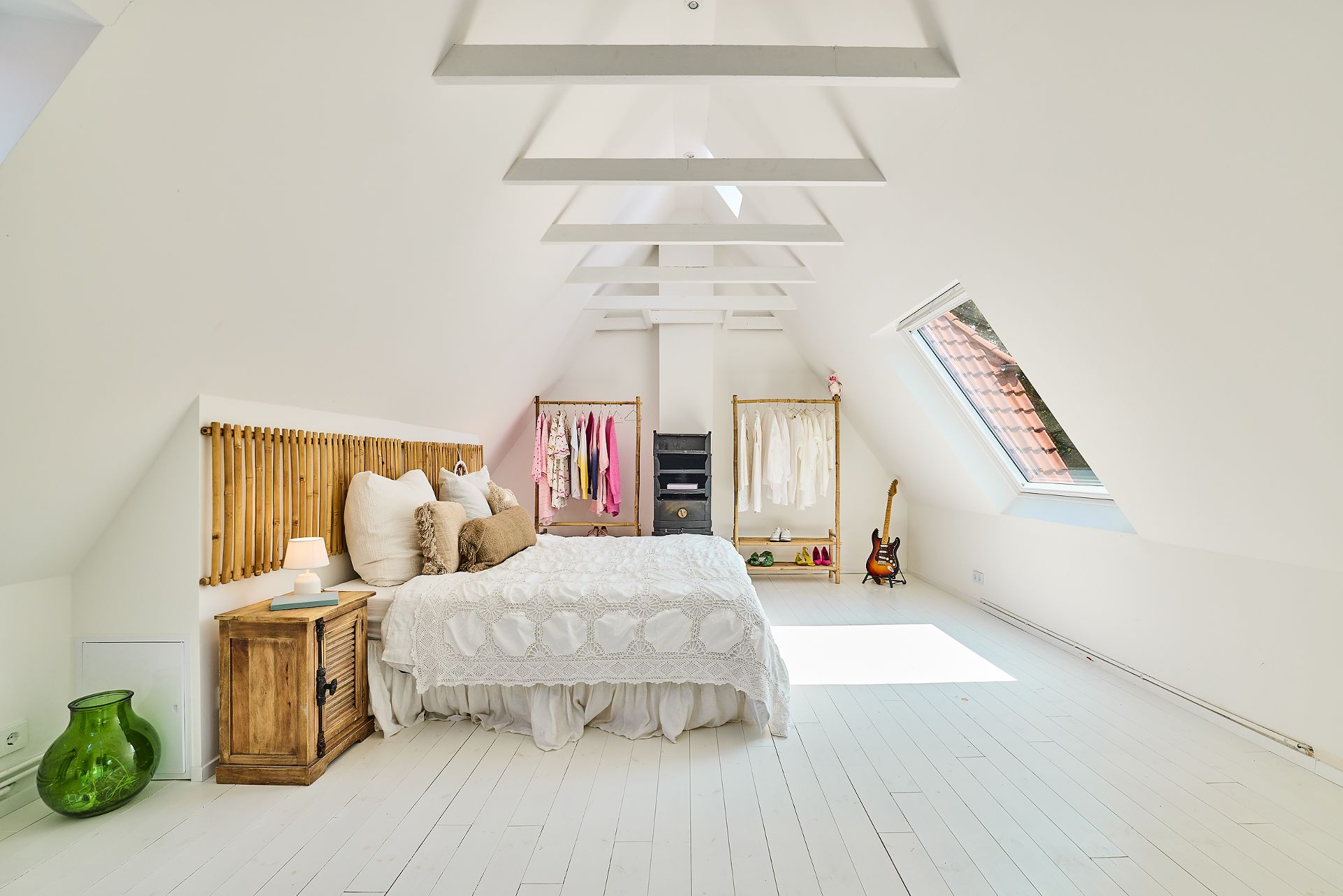 Helles Schlafzimmer im Dachgeschoss mit Bett, Kleiderständern und großem Dachfenster.
