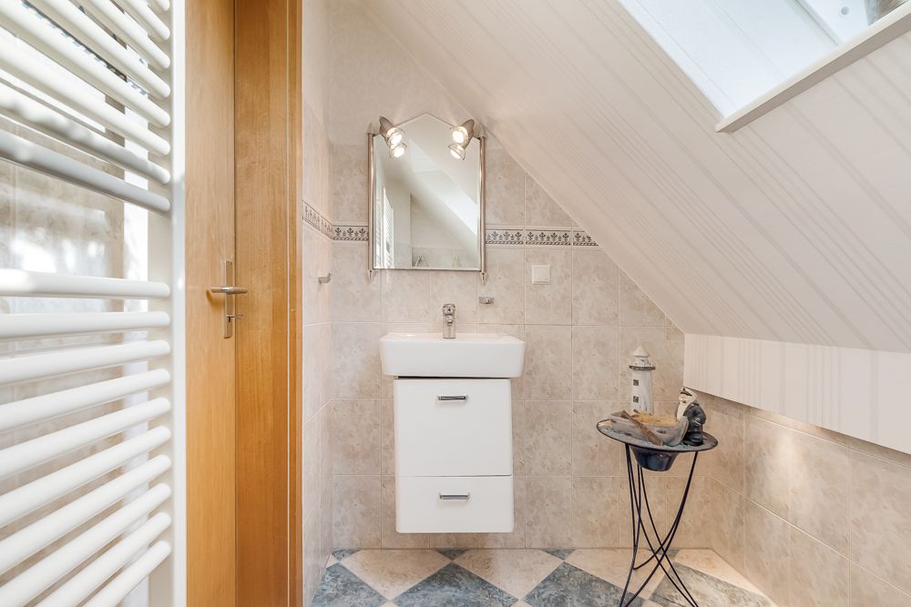 Kleines Badezimmer mit Waschbecken, Spiegel, Dachschräge und Fenster.