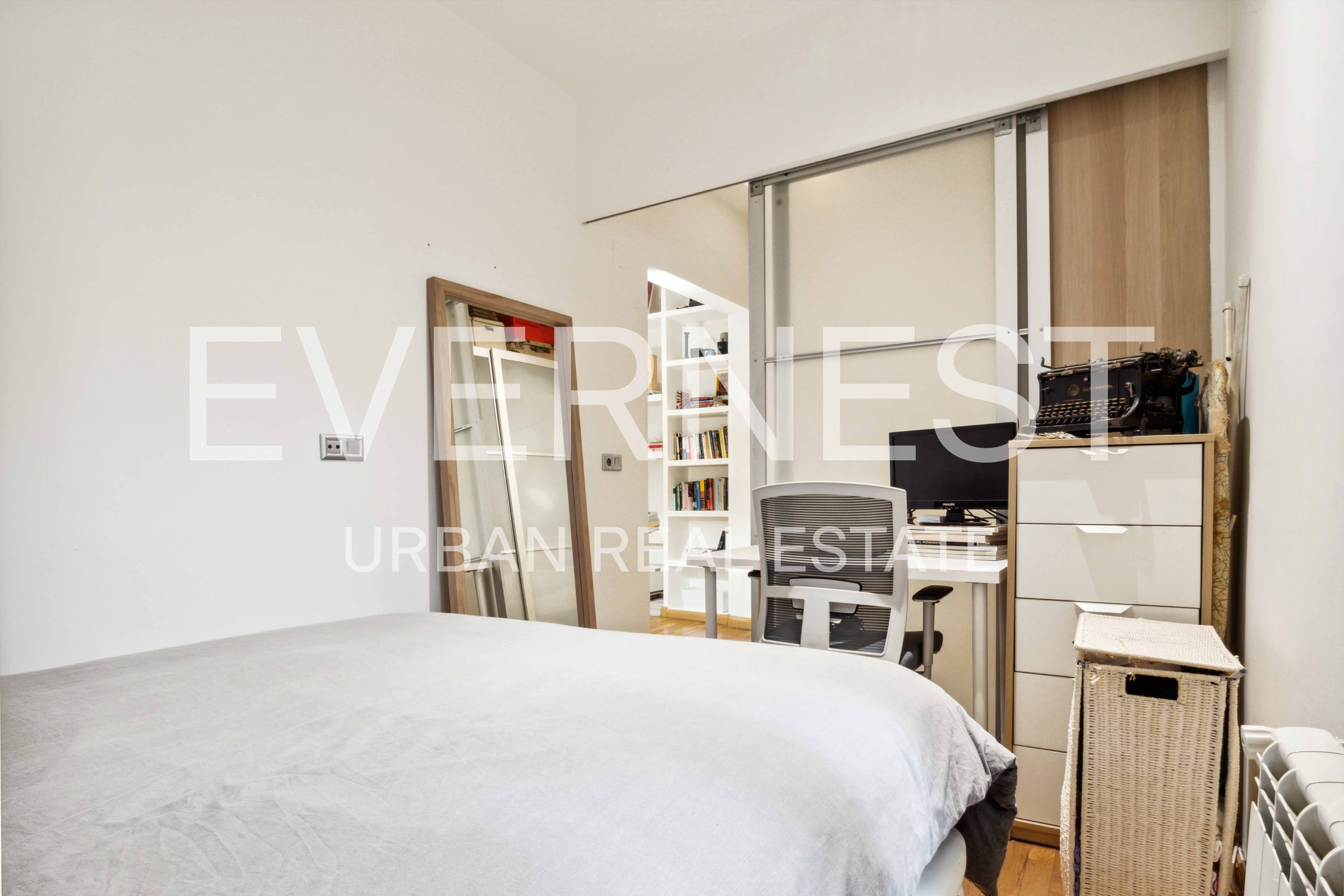 Kleines Schlafzimmer mit Bett, Spiegel, Schreibtisch, Stuhl und Regal mit Büchern.