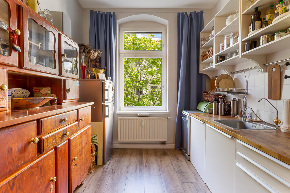 Küche mit Holzmöbeln, weißen Regalen und einem Fenster mit Blick ins Grüne.