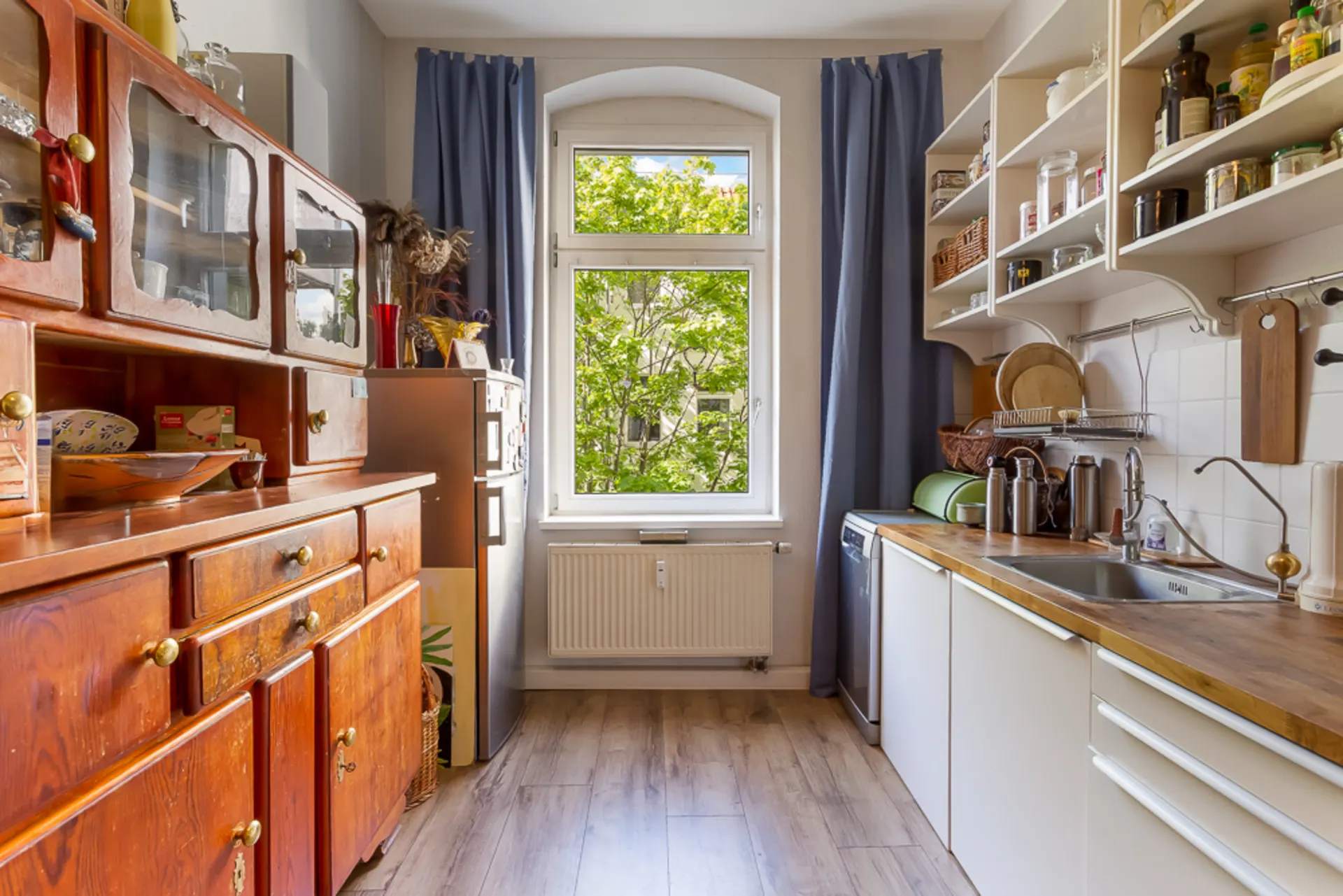 Küche mit Holzmöbeln, weißen Regalen und einem Fenster mit Blick ins Grüne.