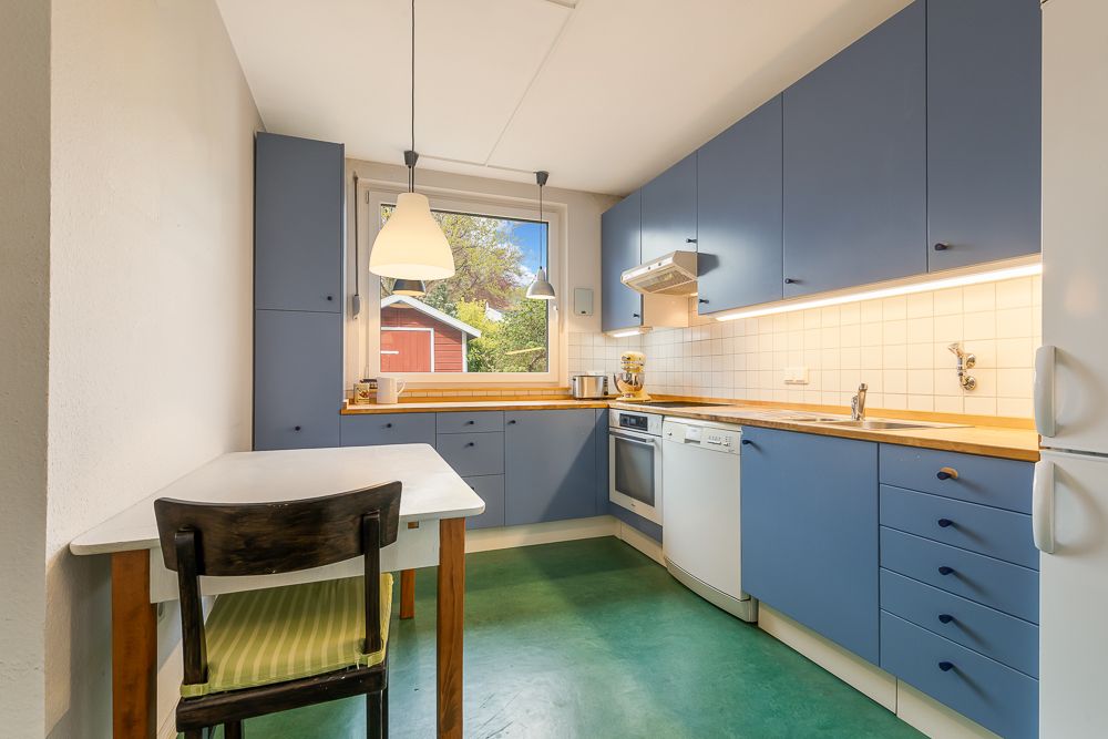 Helle Küche mit blauen Schränken, Holztisch, Stuhl und Fenster mit Blick nach draußen.