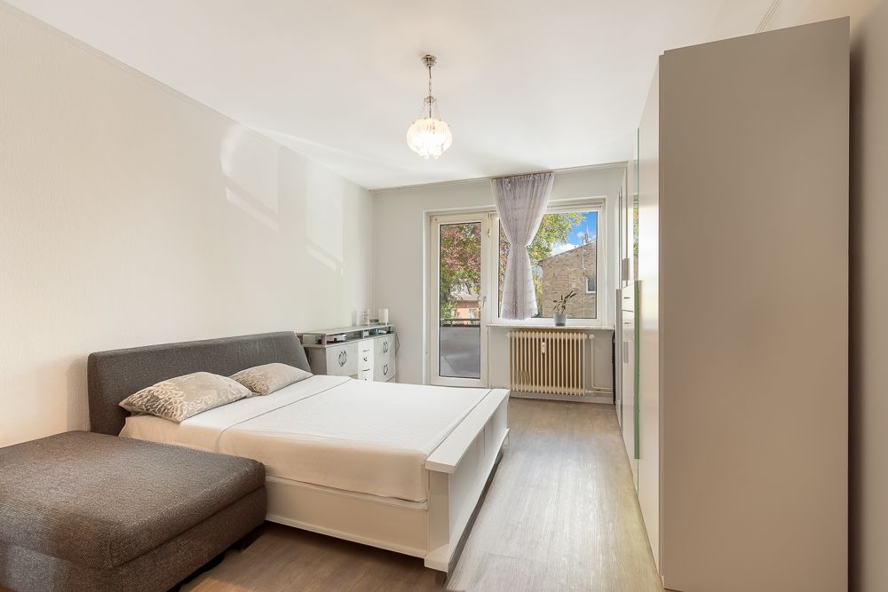 Helles Schlafzimmer mit Doppelbett, Kleiderschrank, Kommode und bodentiefem Fenster.