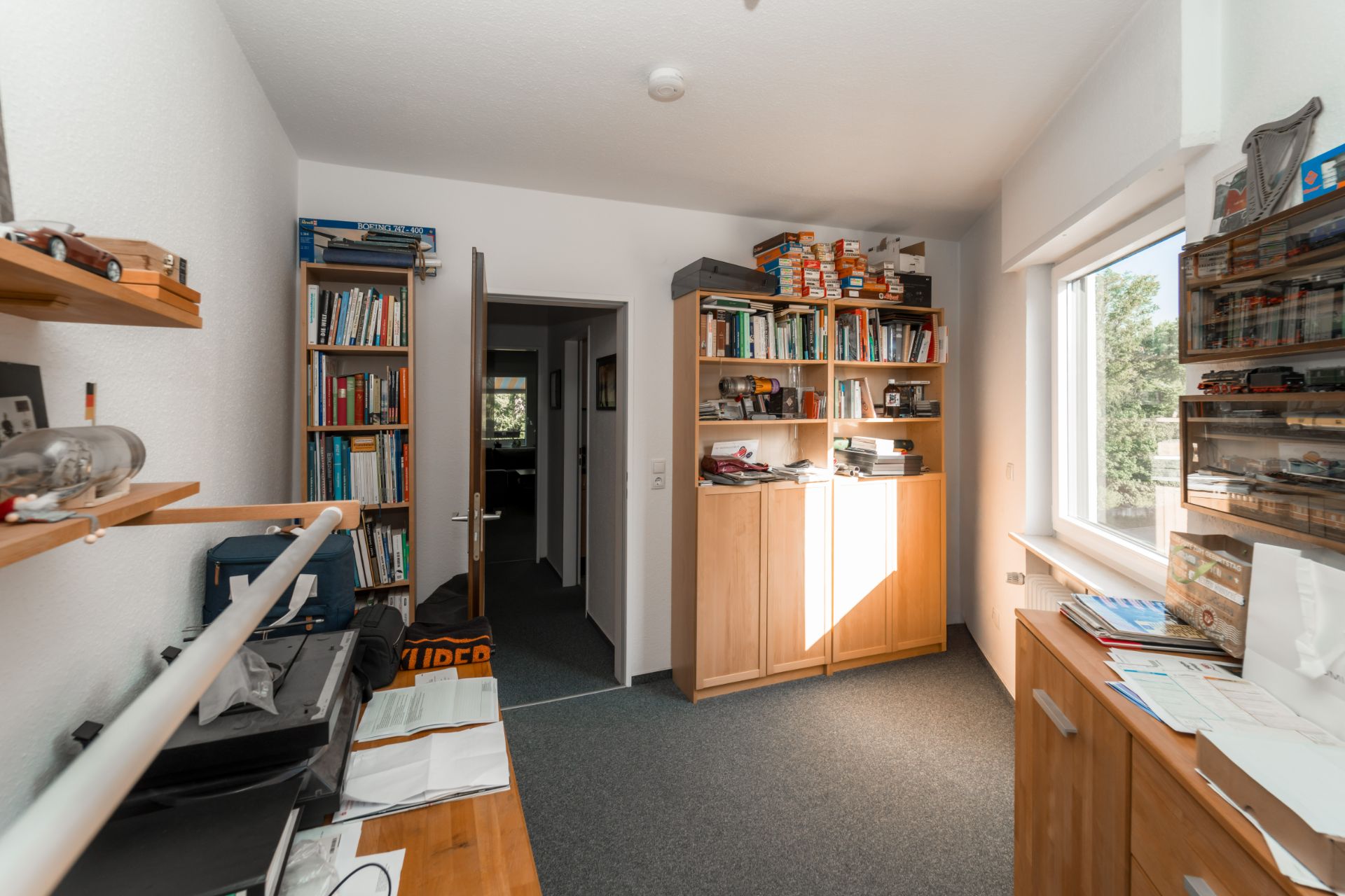 Helles Arbeitszimmer mit Bücherregalen, Schränken, Schreibtisch und großem Fenster.