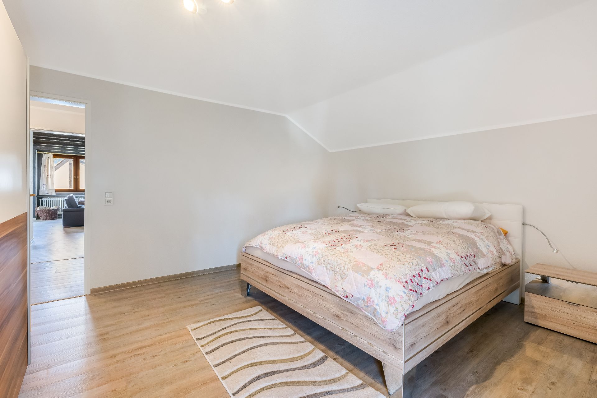 Helles Schlafzimmer mit Doppelbett, Nachttisch und Teppich auf Holzfußboden.