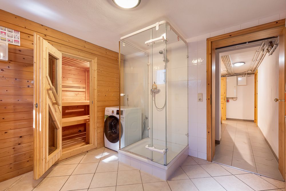 Badezimmer mit Sauna, Duschkabine und Waschmaschine, gefliestem Boden und Holzwänden.
