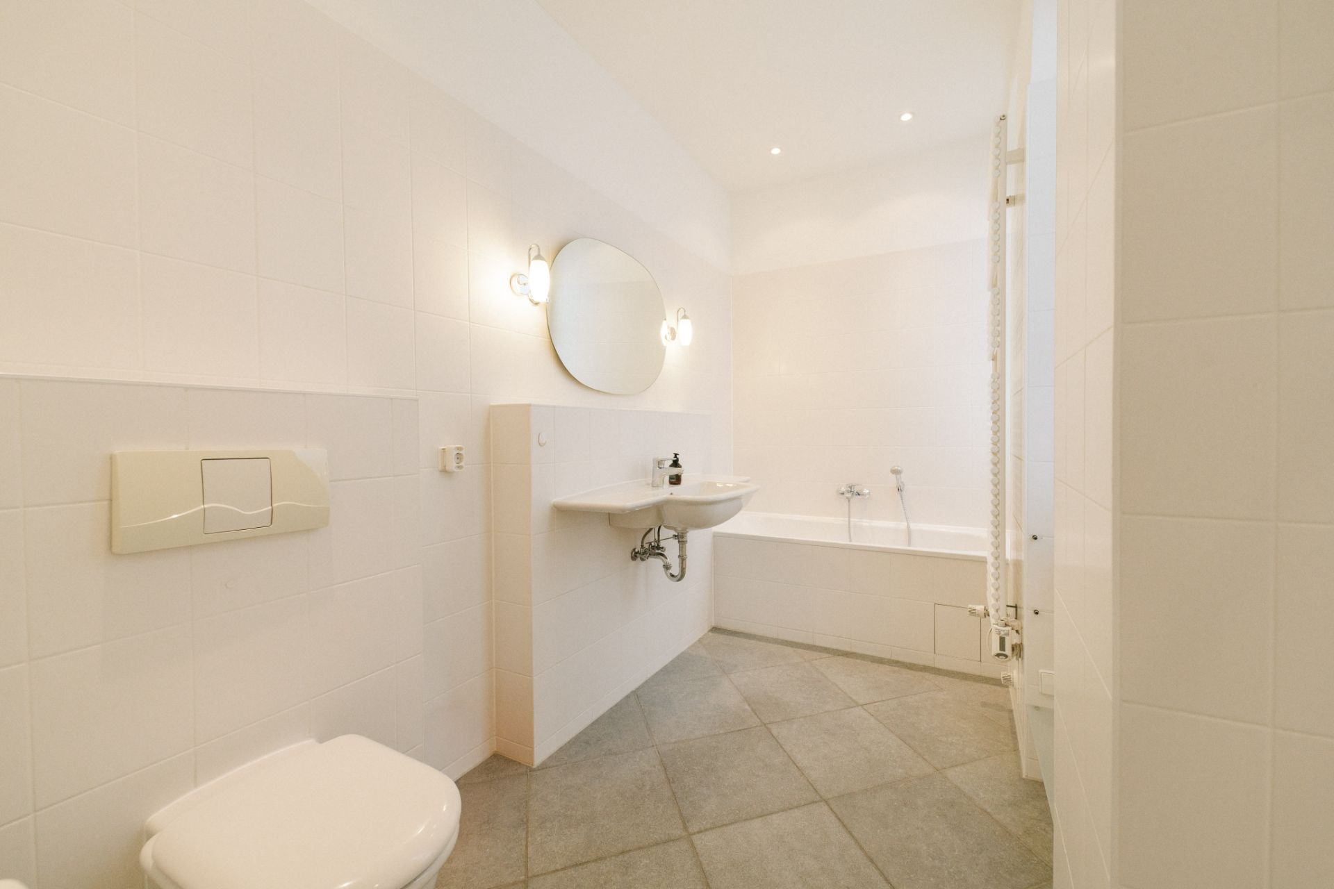 Helles Badezimmer mit WC, Waschbecken, Spiegel und Badewanne.