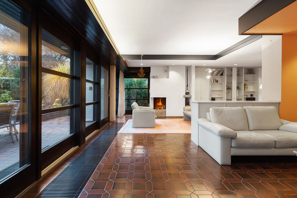 Modernes Wohnzimmer mit weißen Sofas, Kamin, großen Fenstern und Blick auf Terrasse.