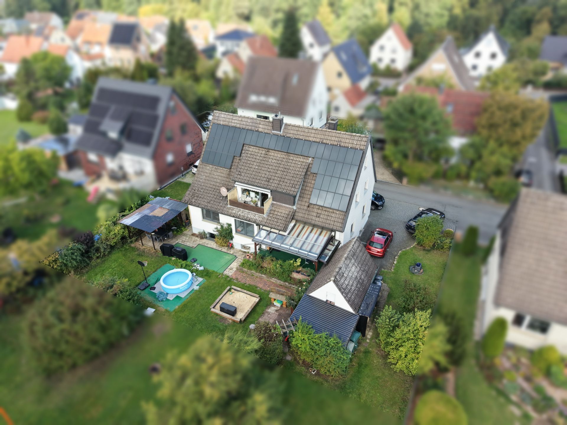 Luftbild von einem Einfamilienhaus mit Garten, Pool, Terrasse und Einfahrt.