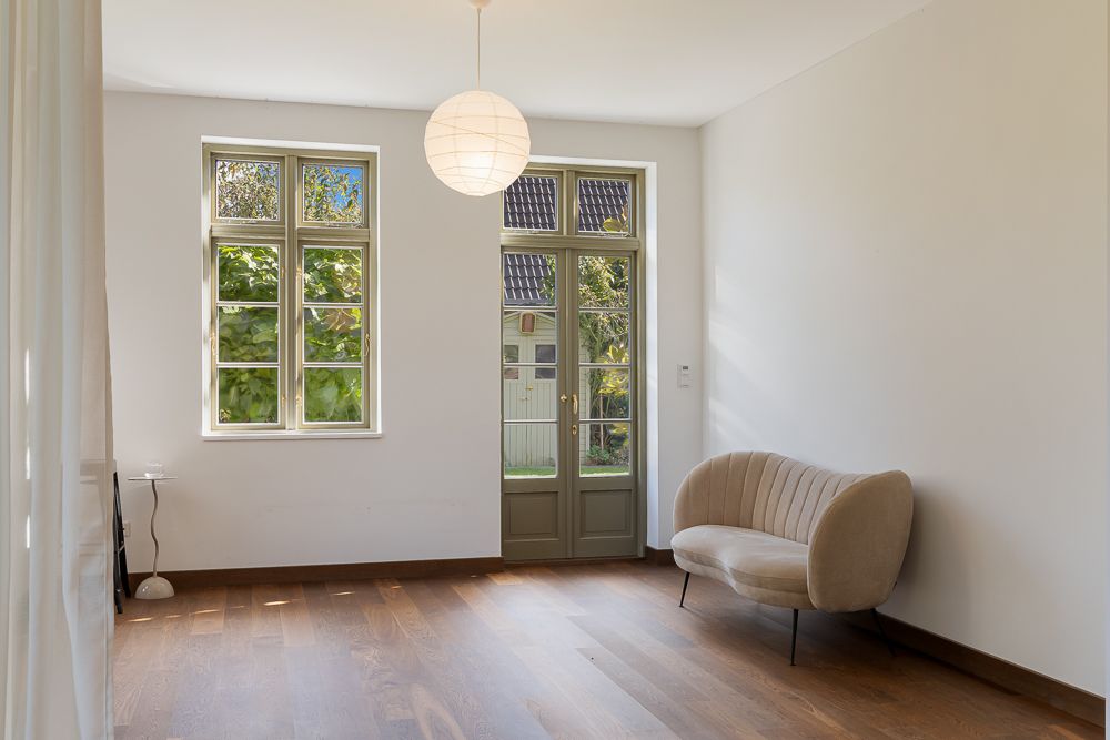 Helles Wohnzimmer mit Holzfußboden, Sofa, Fenster und Glastür mit Blick nach draußen.
