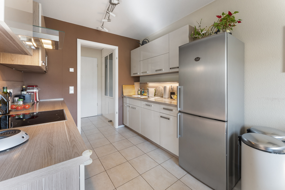 Moderne Küche mit brauner Wand, weißen Schränken, großem Kühlschrank und Pflanzen darauf.