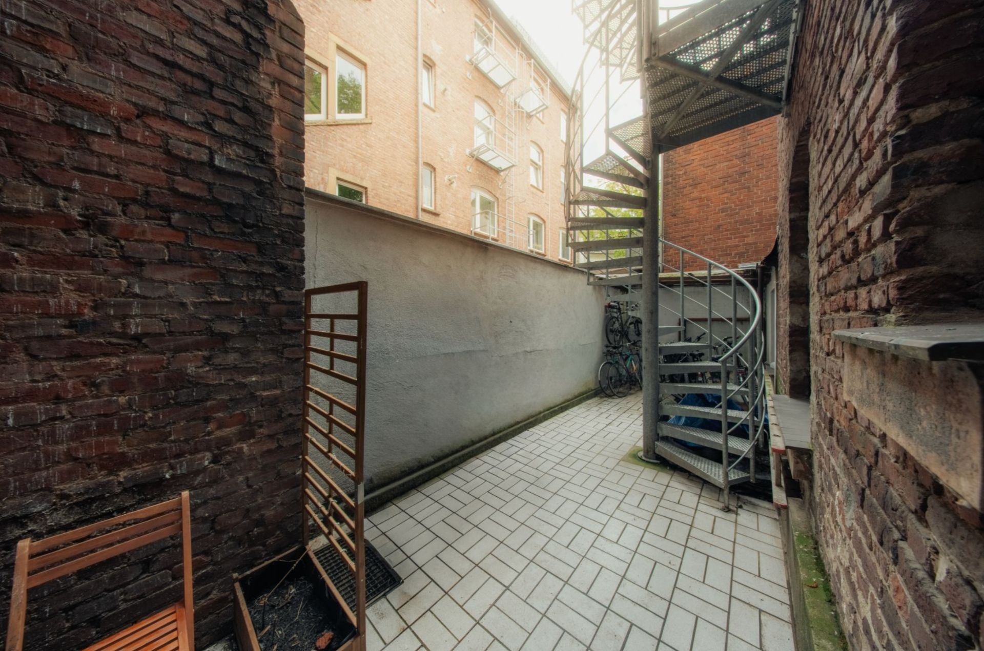 Kleiner, gefliester Innenhof mit Backsteinwänden und einer Metallwendeltreppe.