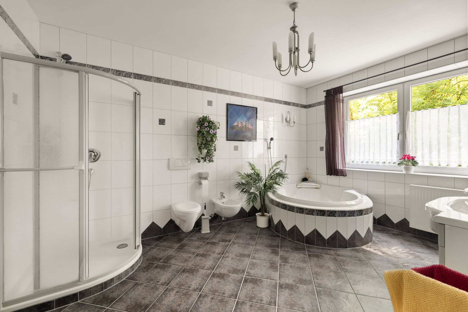 Modernes Badezimmer mit Dusche, Badewanne, WC und großen Fenstern, dekoriert mit Pflanzen.