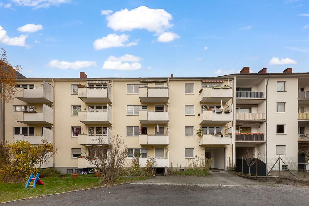 Mehrfamilienhaus mit mehreren Balkonen und kleinem Spielplatz im Vordergrund.