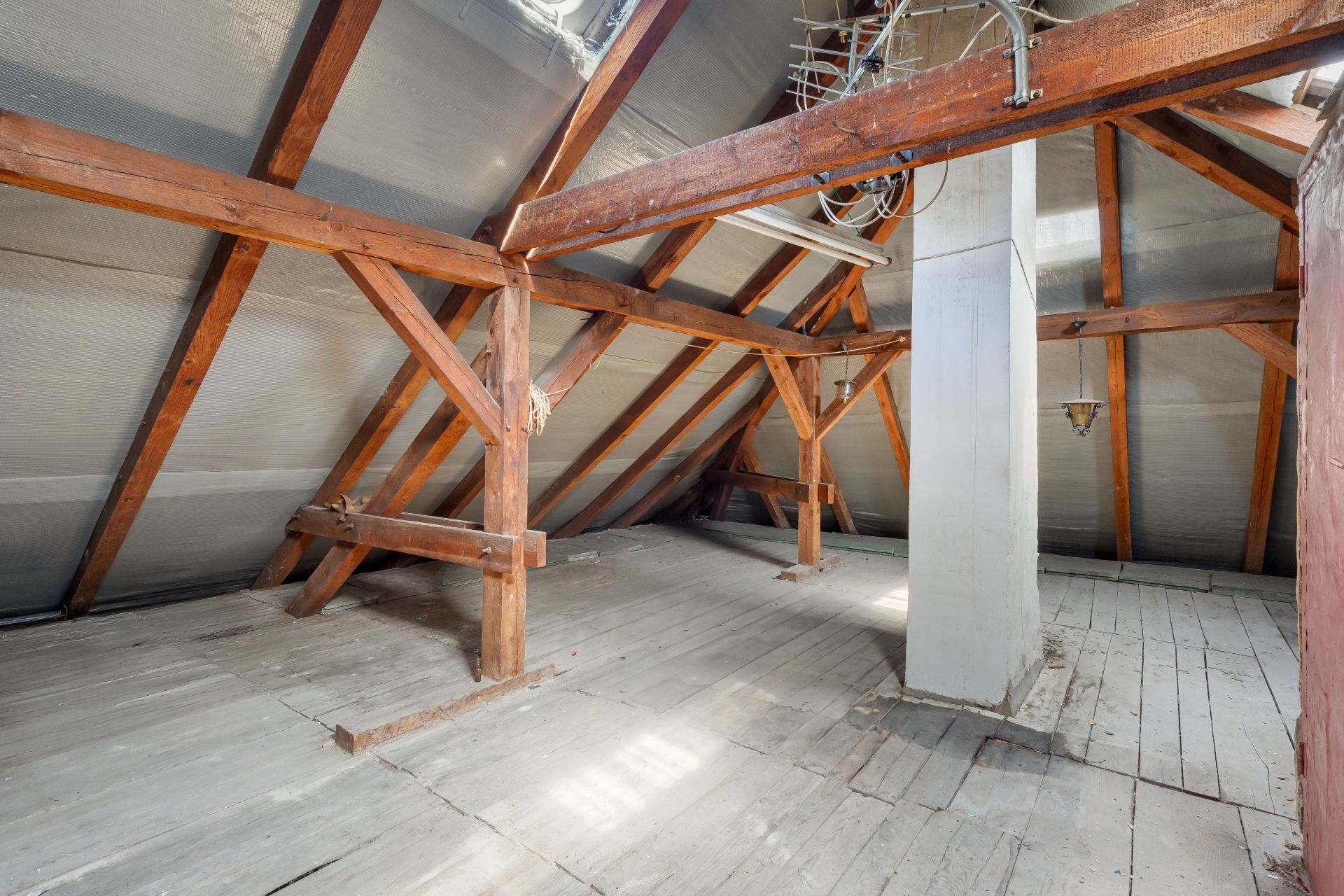 Leerer Dachboden mit Holzbalken, Holzfußboden und einem weißen Kamin in der Mitte.