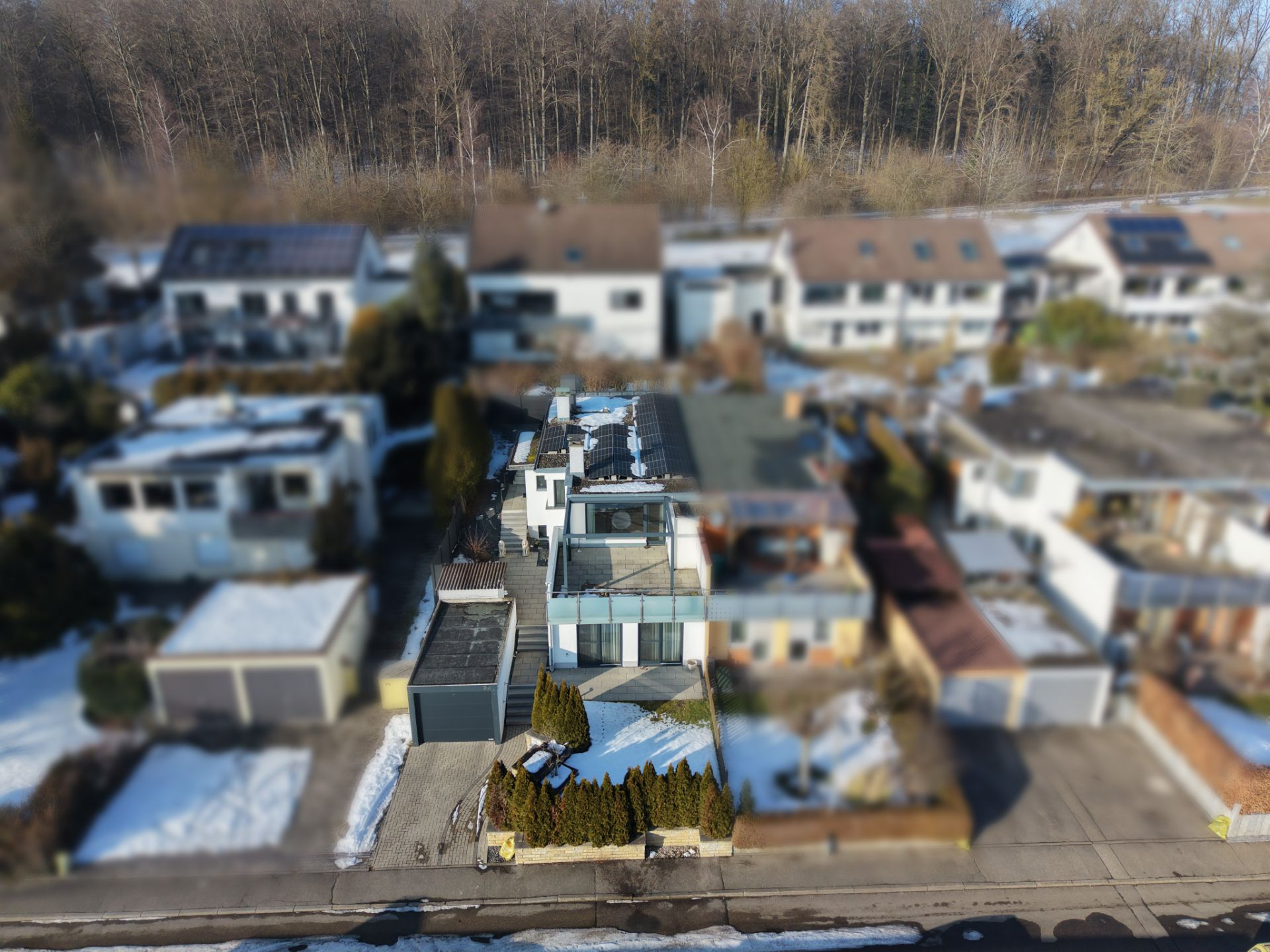 Luftaufnahme eines modernen Einfamilienhauses mit Garten und Einfahrt im Wohngebiet, teils mit Schnee bedeckt.