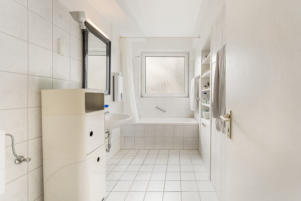 Helles Bad mit Badewanne, Waschbecken, Spiegel und Regal, Fenster mit Milchglas.