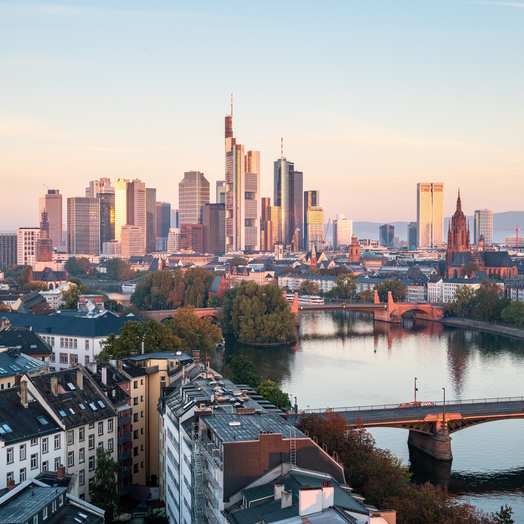 Blick auf Hochhäuser, Fluss und Brücken in einer Stadt bei Sonnenuntergang.