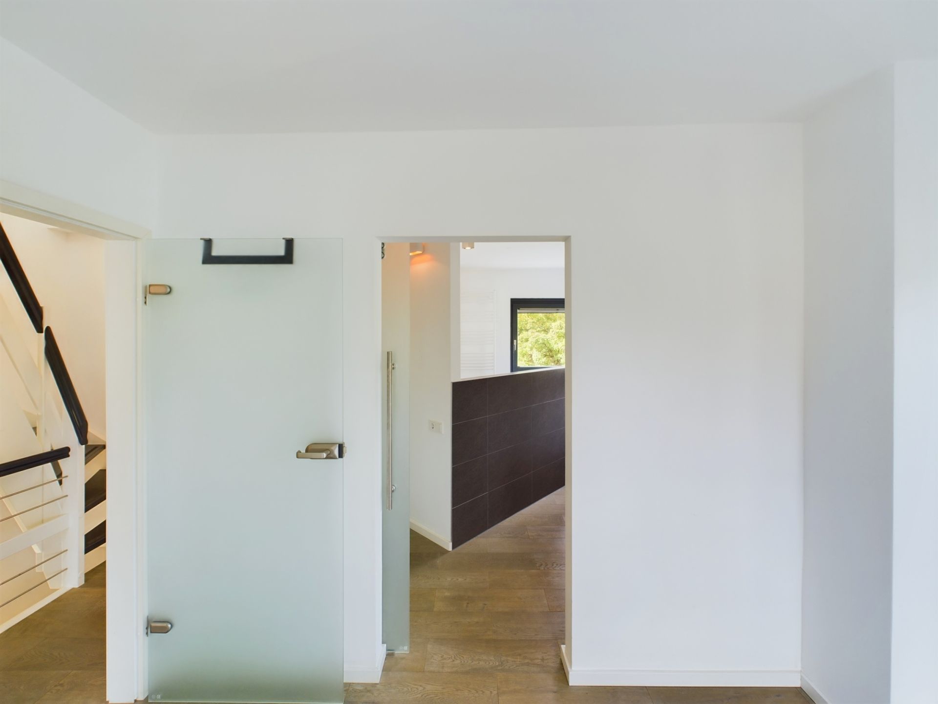 Flur mit Glastür, Holzboden und Treppe mit weißem Geländer.