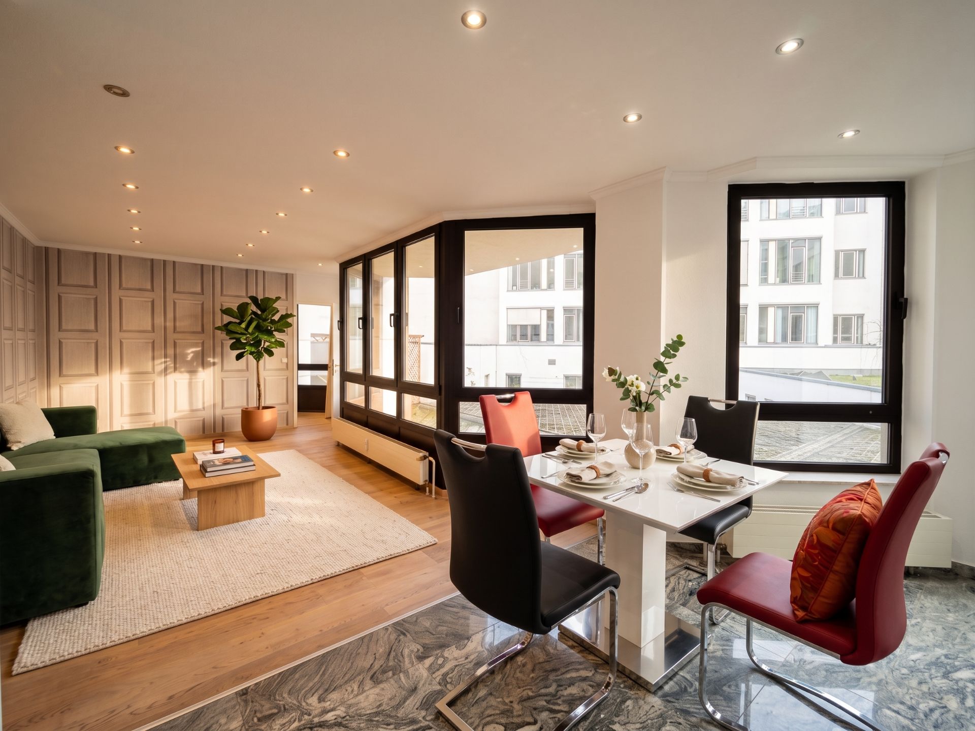 Helles Wohnzimmer mit grünem Sofa, Esstisch und großen Fenstern, moderner Einrichtungsstil.