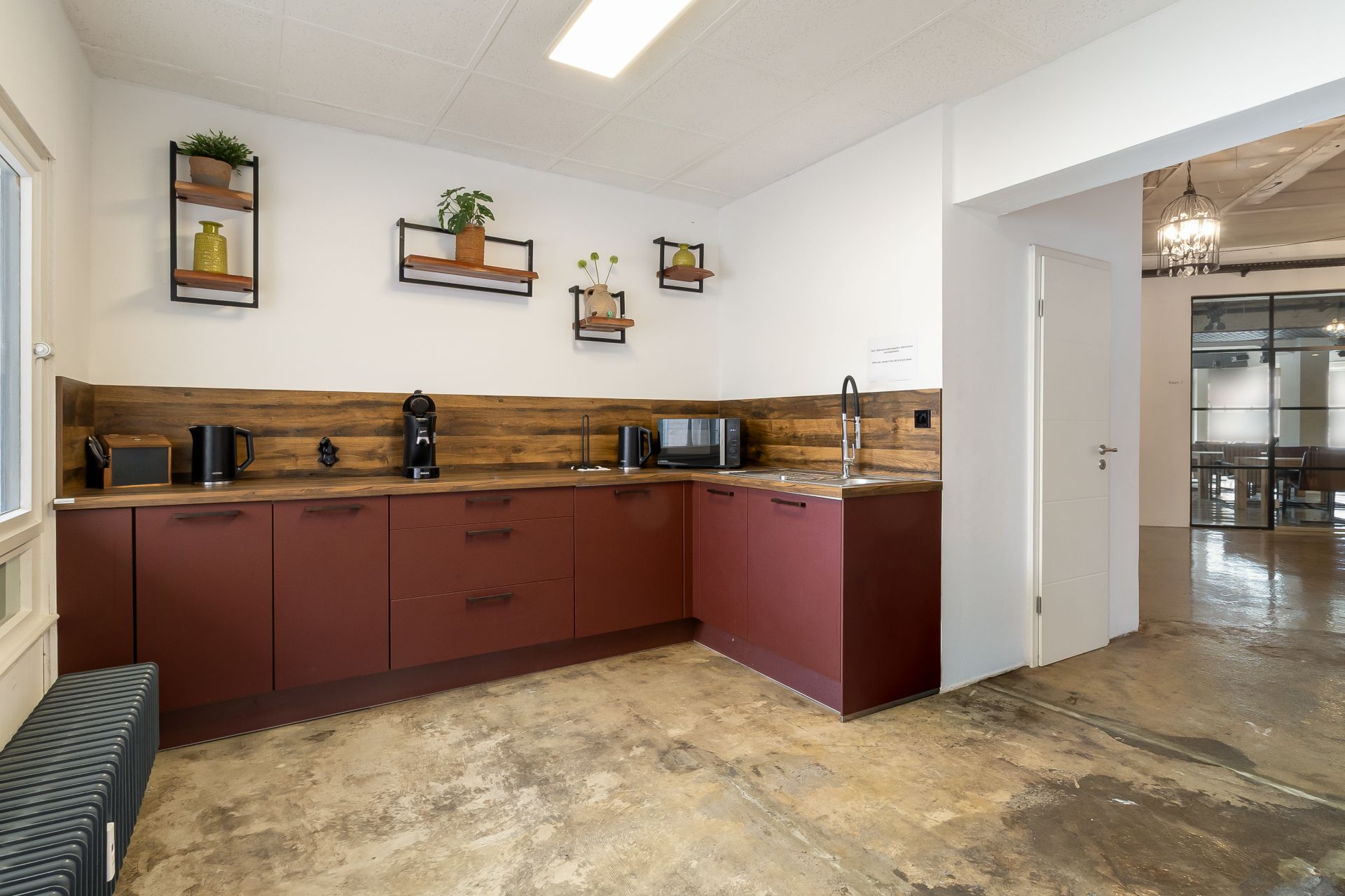 Moderne Küche mit roten Schränken, Holzwand und Geräten, Wandregale mit Pflanzen.