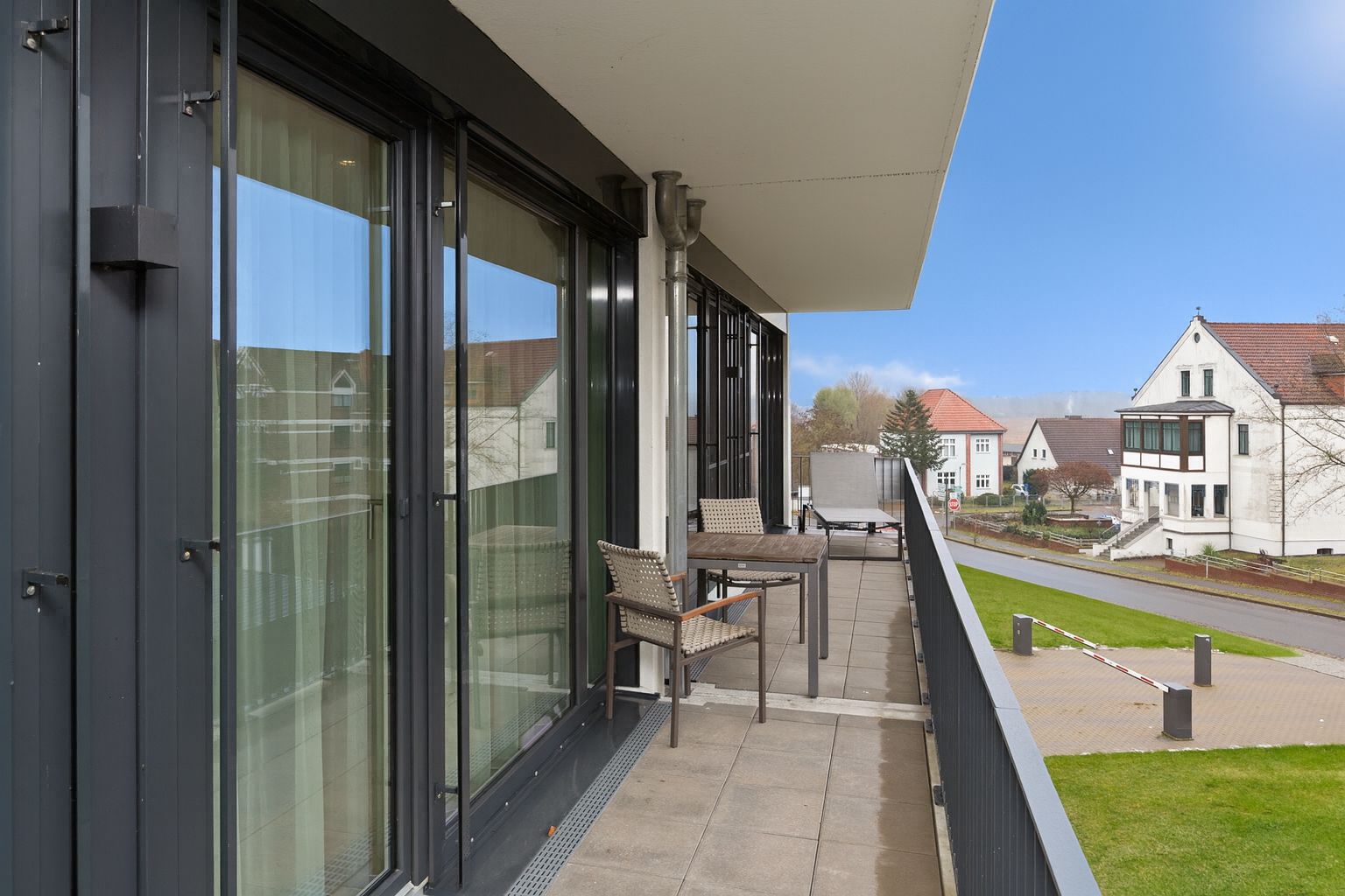 Großer Balkon mit Tisch und Stühlen, Blick auf Straße und Wohnhäuser.