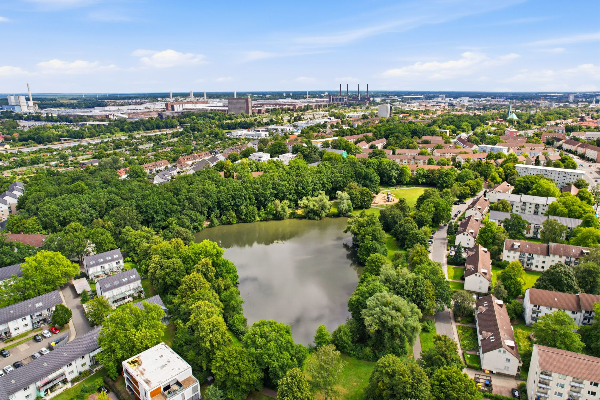 Luftbild einer Wohngegend mit Teich und vielen Bäumen zwischen den Häusern.