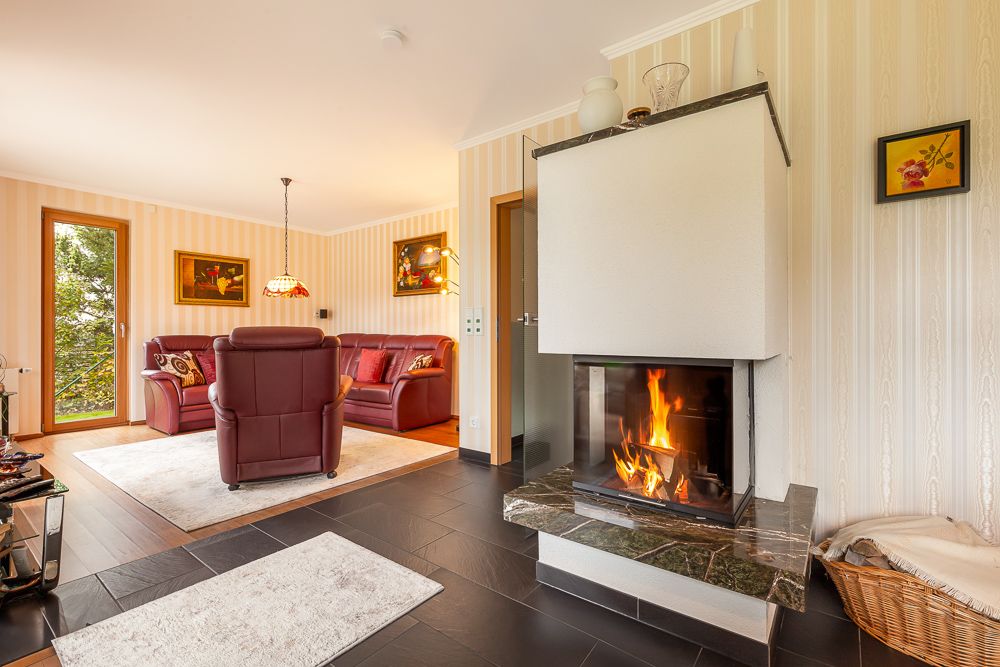 Helles Wohnzimmer mit Kamin, roten Ledersofas und großen Fenstern, Teppiche auf dunklem Boden.