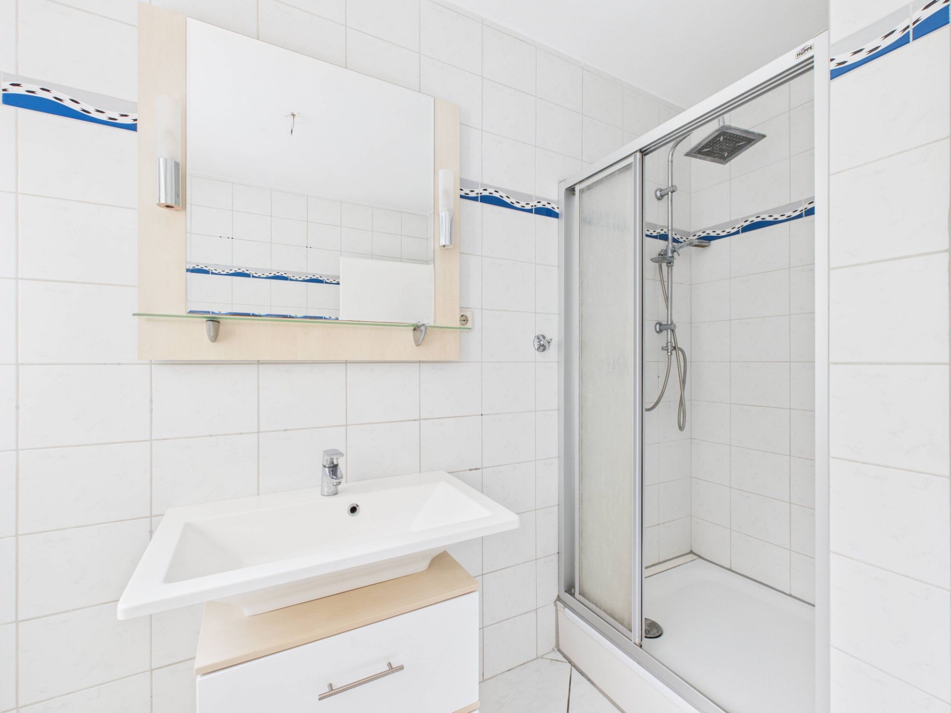 Helles Badezimmer mit Waschbecken, Spiegel und Dusche mit Glastür.