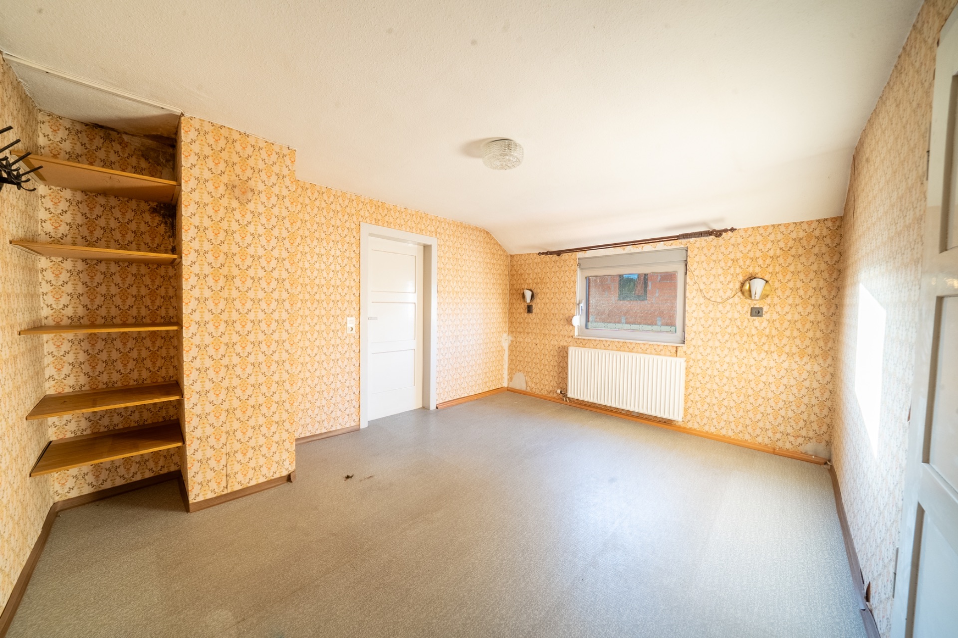 Leerer Raum mit Tapeten, Regal an der Wand, Fenster, Tür und Heizkörper.
