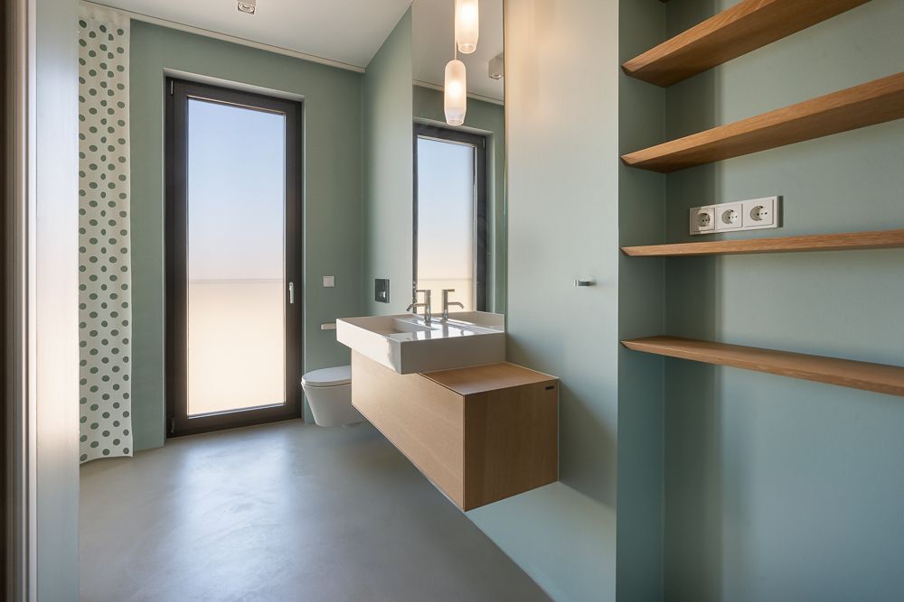 Modernes Badezimmer mit großem Fenster, Waschbecken, Wandregalen und Toilette.
