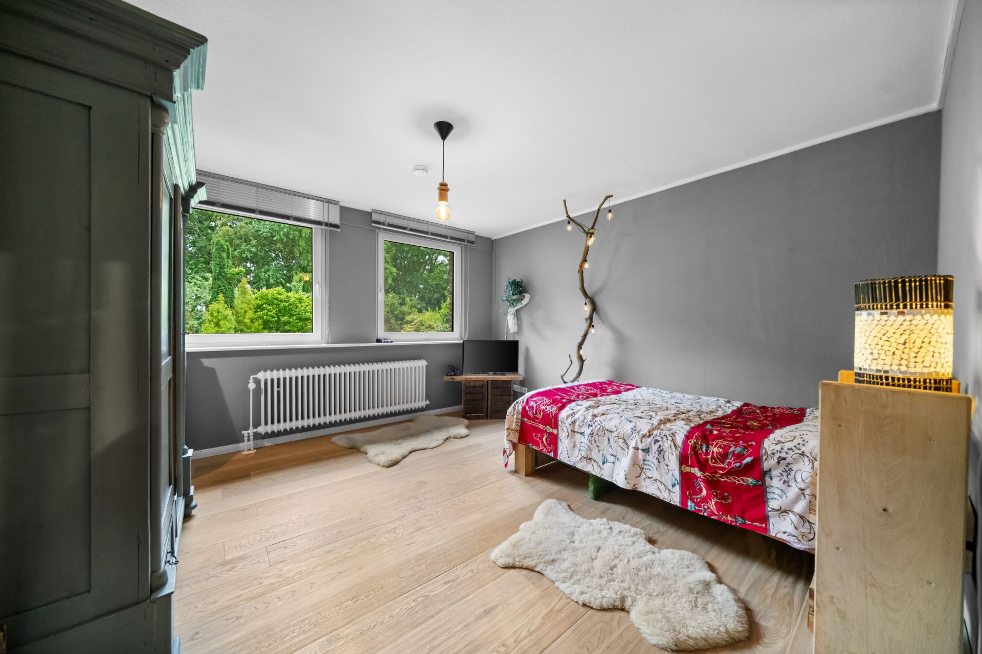 Schlafzimmer mit Einzelbett, Holzboden, großem Fenster und grauen Wänden.