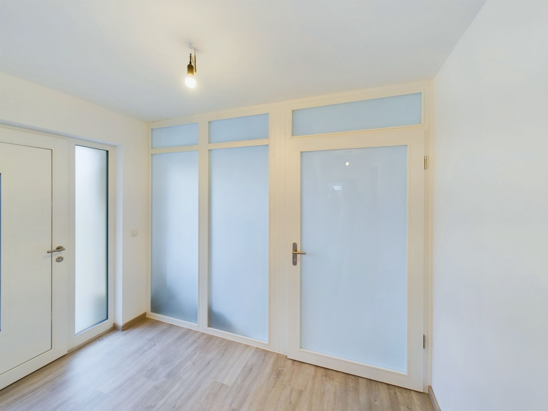 Heller Raum mit Holzboden, Glastüren und matten Glaspaneelen.