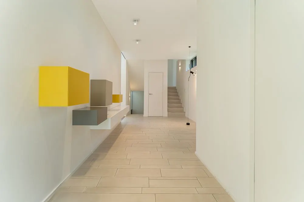 Heller Flur mit Wandregalen in Gelb und Grau, hinten Treppe und Tür sichtbar.