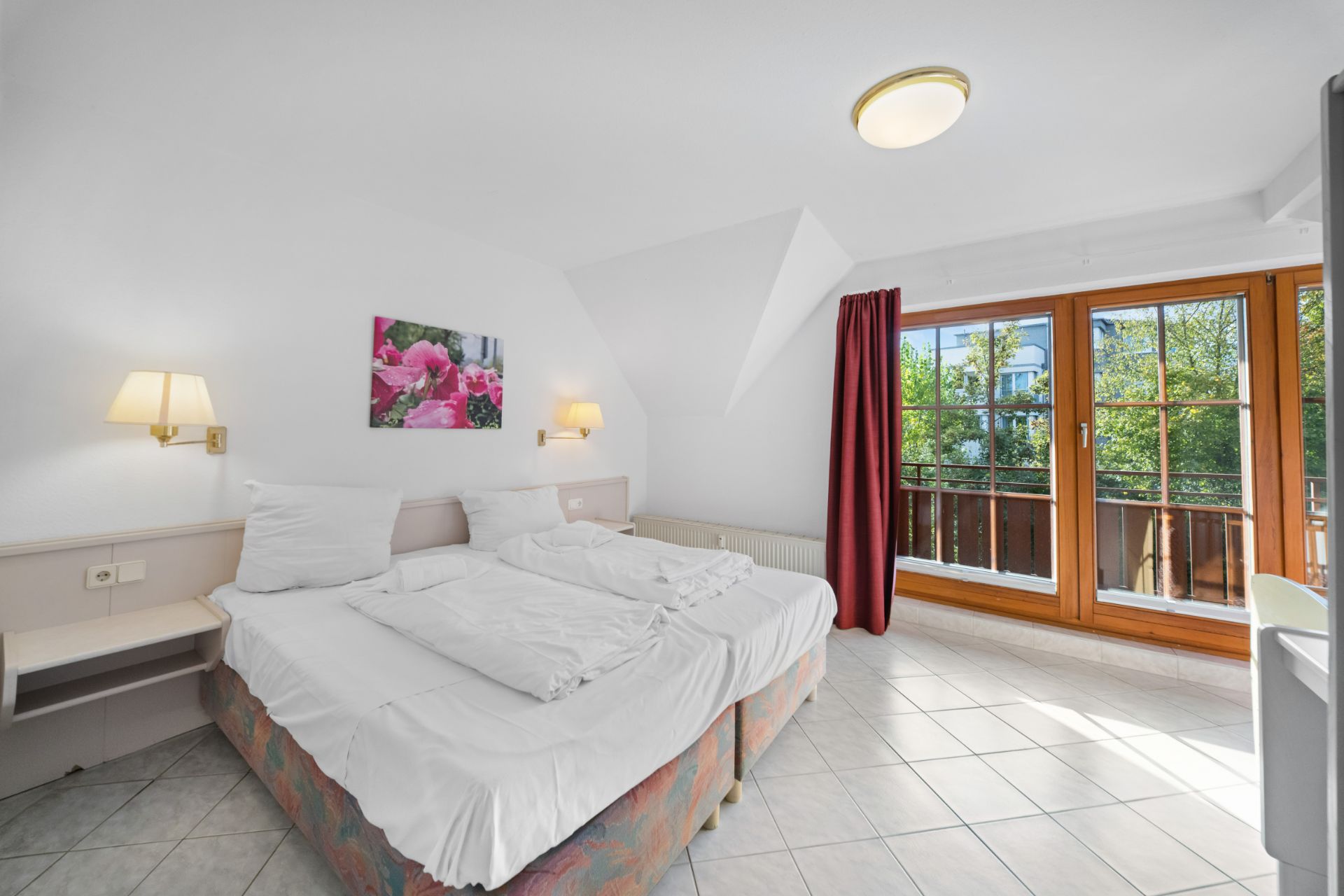 Helles Schlafzimmer mit Doppelbett, Nachttischen, Balkontür und Wandbild mit Blumenmotiv.
