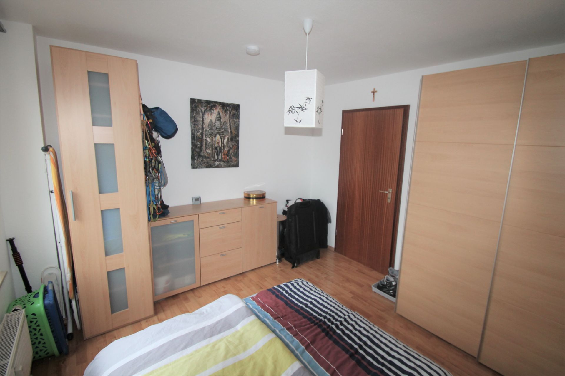Helles Schlafzimmer mit Holzboden, Schrank, Kommode, Bett und Tür.