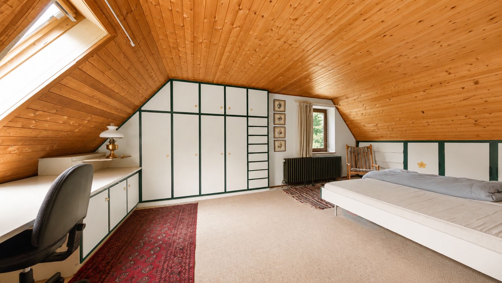 Dachzimmer mit Holzdecke, Einbauschränken, Schreibtisch, Stuhl, Bett und Teppichen.