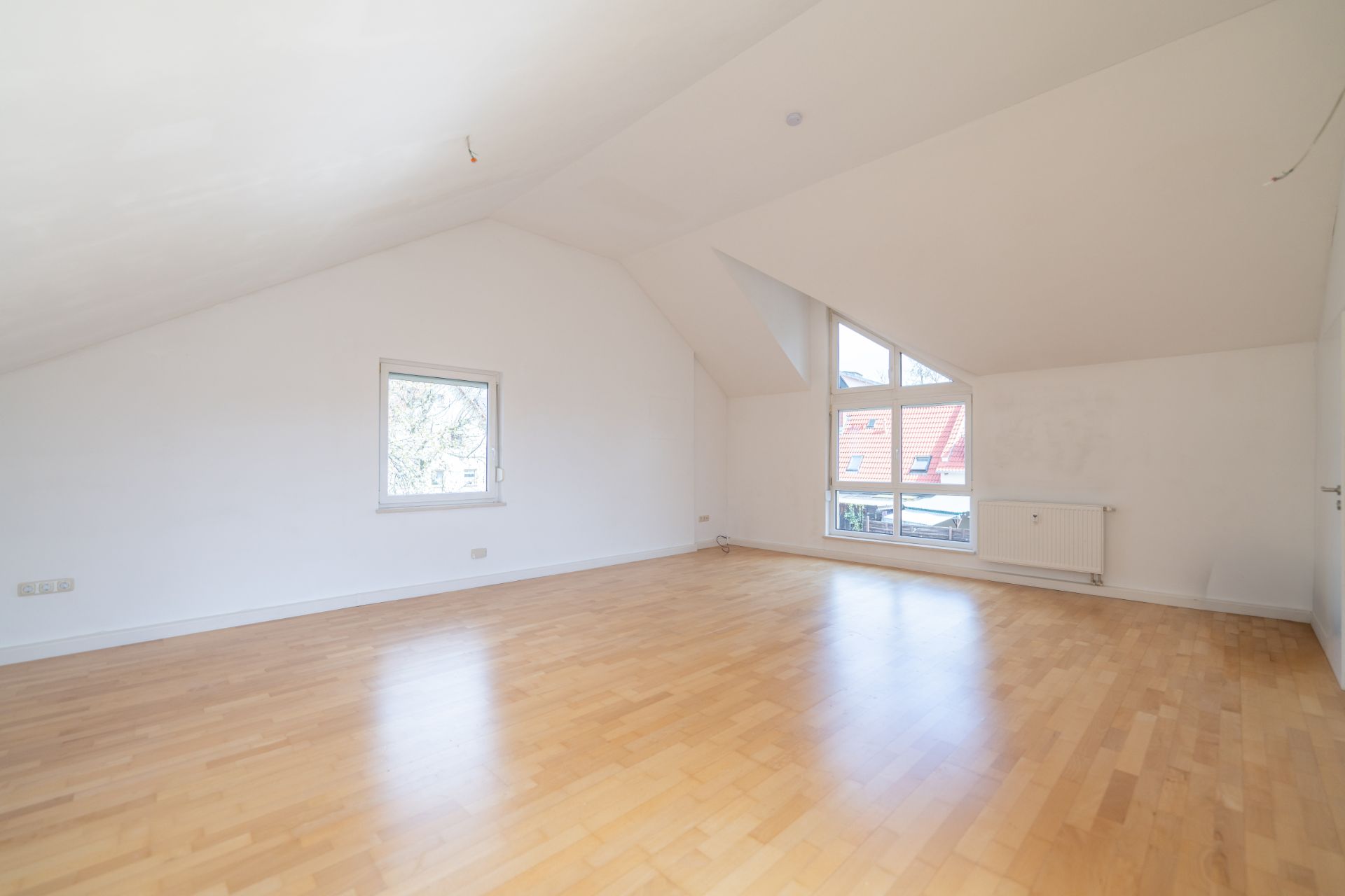 Leerer Dachgeschossraum mit Parkettboden, weiß gestrichenen Wänden und großen Fenstern.