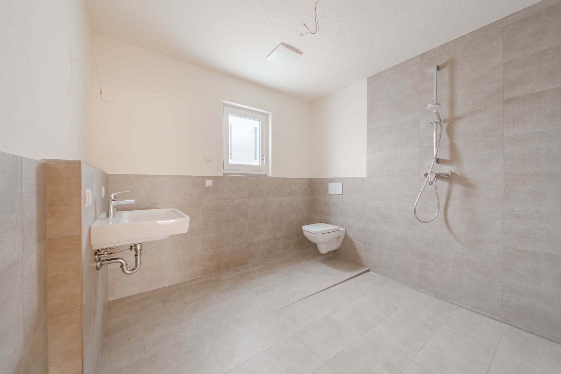 Barrierefreies, modernes Bad mit Dusche, Wand-WC, Fenster und Waschbecken.