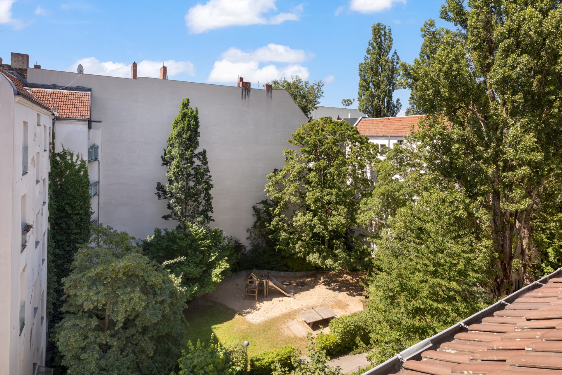 Blick auf einen begrünten Innenhof mit Bäumen und einem kleinen Spielplatz mit Sandfläche.