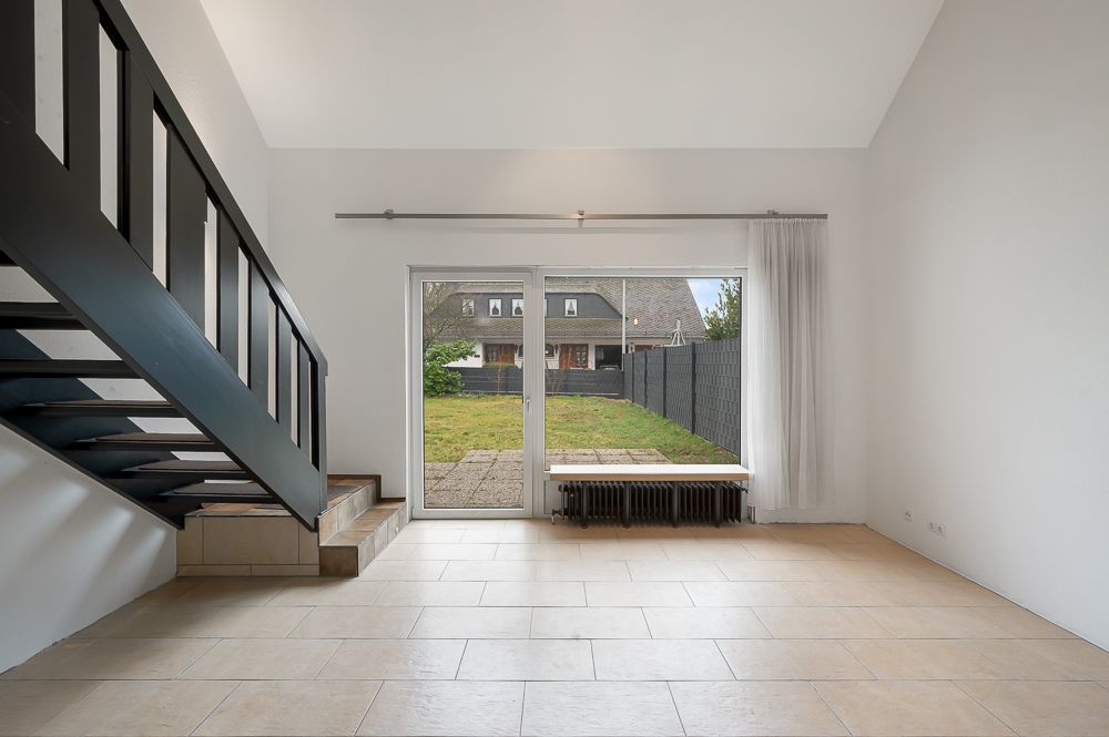 Helles Wohnzimmer mit Fliesenboden, Treppe und großer Glastür zum Garten.