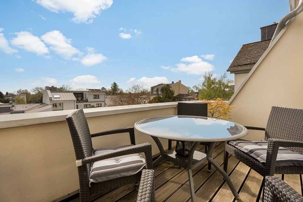 Balkon mit rundem Glastisch und vier geflochtenen Stühlen, Blick auf Nachbarhäuser.