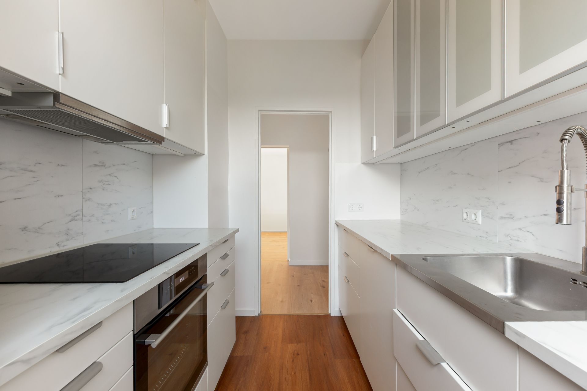 Moderne, schmale Küche mit weißen Schränken, Herd, Backofen und Edelstahlspüle.
