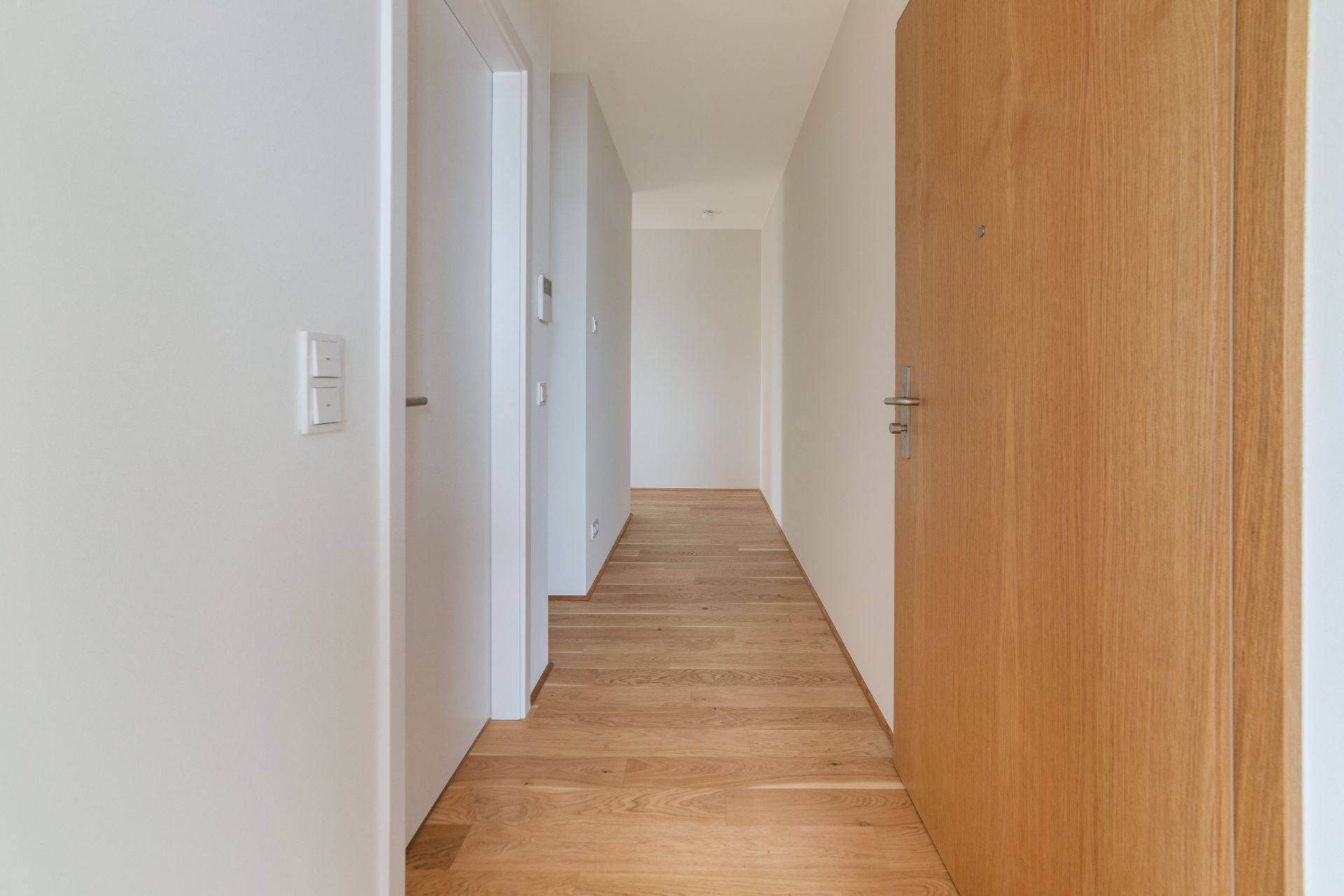 Heller Flur mit Holzboden, weißen Wänden und mehreren geschlossenen Türen.
