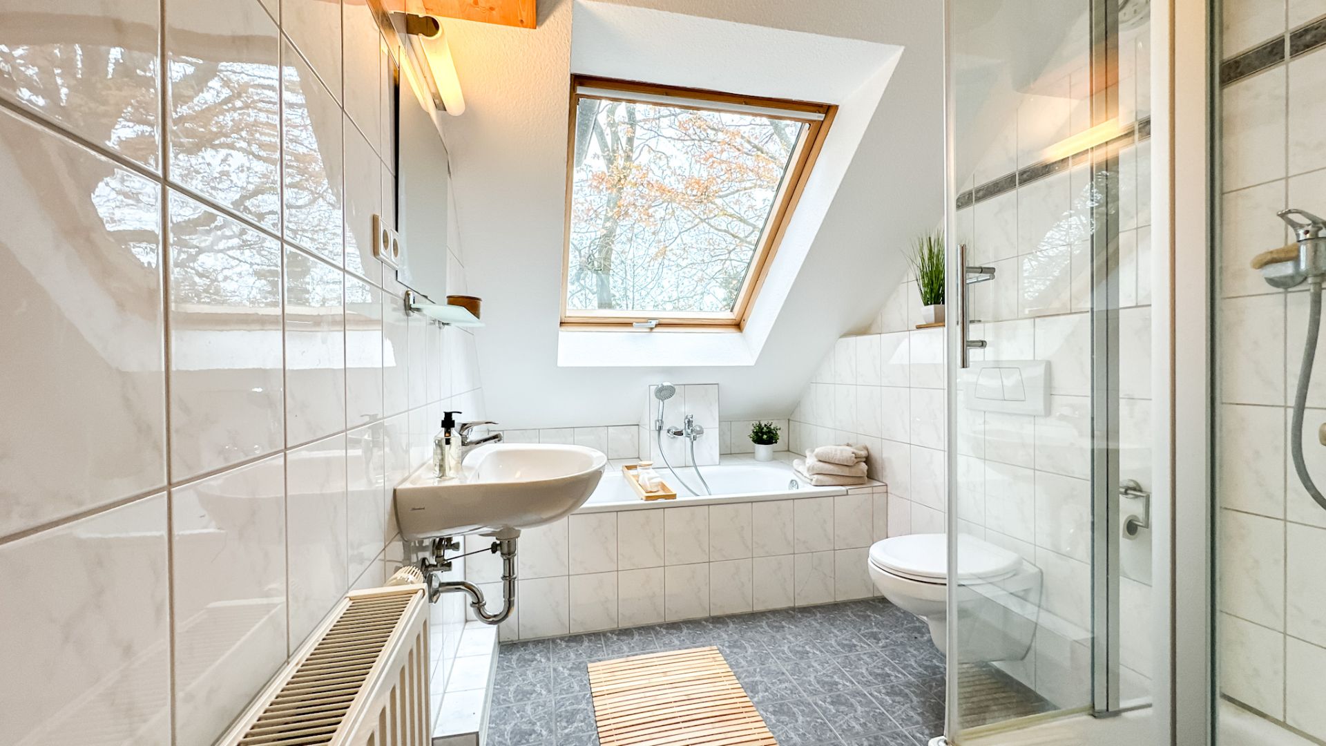 Helles Badezimmer mit Dachfenster, Badewanne, Waschbecken, Toilette und Dusche.