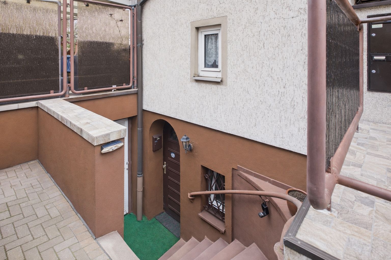 Abwärts führende Außentreppe zu einer braunen Haustür mit kleinem Fenster und Laterne.