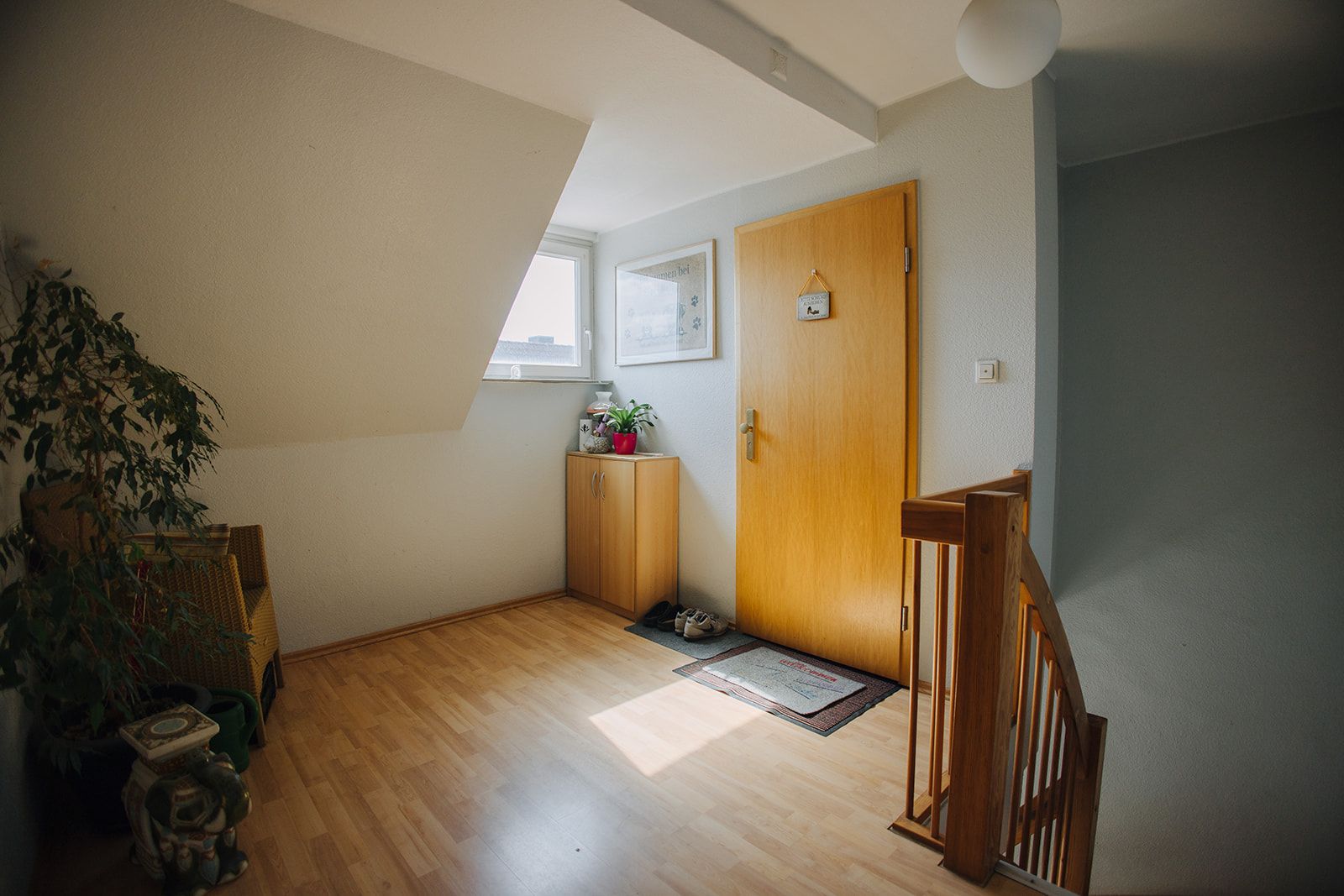 Heller Flur mit Holztür, Fenster, Pflanze, kleinem Schrank und Treppe.